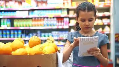 在杂货店买数字平板电脑的小女孩在网上买橘子水果。 超市里的小女孩